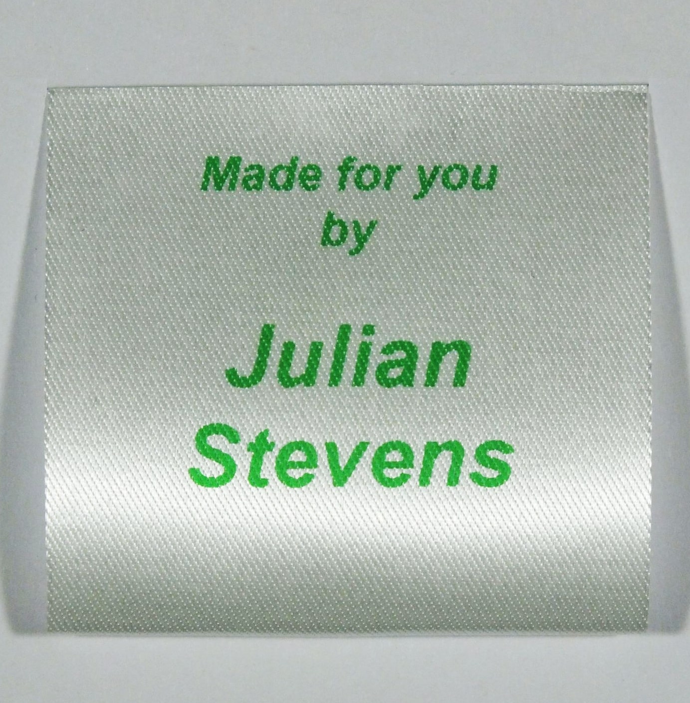 A sew in personalised clothing label printed in Green on Silvery White material