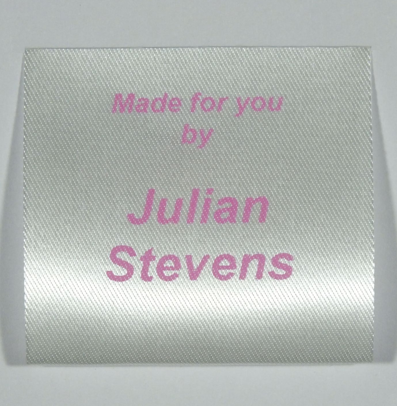 A sew in personalised clothing label printed in Pink on Silvery White material