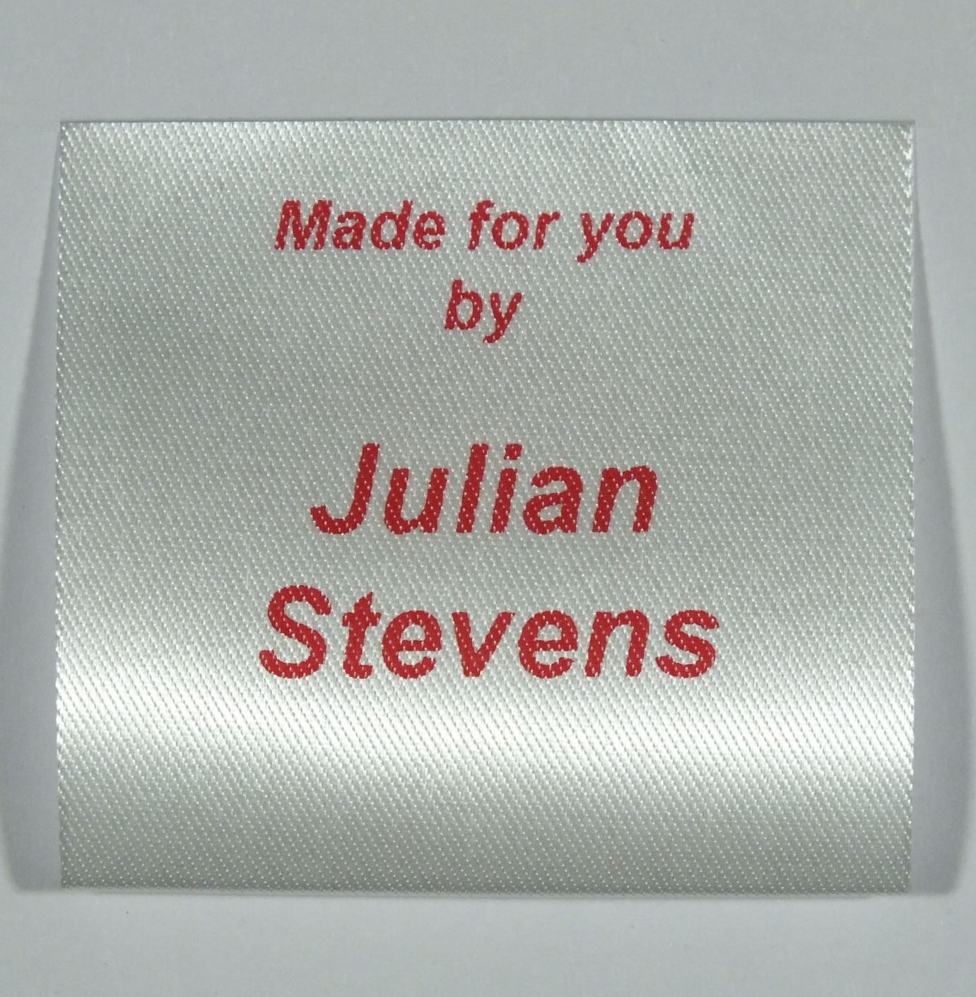 A sew in personalised clothing label printed in Red on Silvery White material