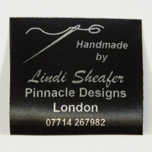 A Black sew in personalised Garment label with Silver print featuring a needle and cotton design.